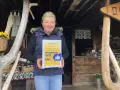 Kobieta z certyfikatem "Przejściowa Firma" przed bacówką. W tle widać rękodzieło i przetwory, a także tablicę z napisem "Bacówka u Jancora".