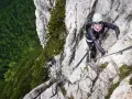 Kobieta wspina się po via ferrata w Dolomitach, z widokiem na gęsty las poniżej.