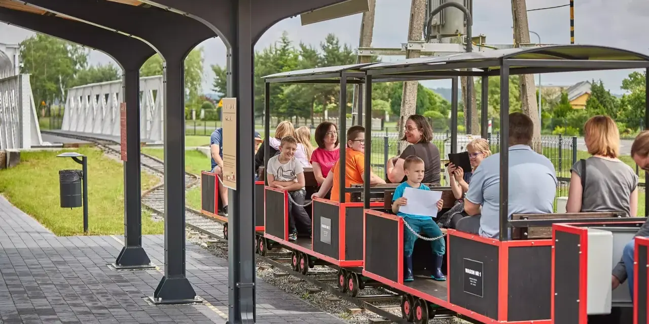 Wesołe roztocze z dziećmi podróżują kolejką. Uśmiechnięte twarze, słońce i zielone krajobrazy tworzą radosną atmosferę.