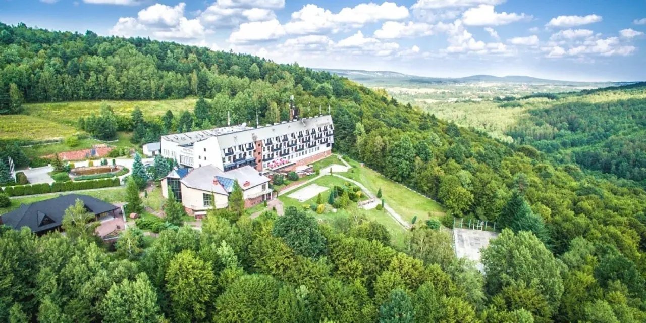 Hotel w otoczeniu zielonych lasów Gór Świętokrzyskich, blisko Kielc. Widok z lotu ptaka na budynki i krajobraz.