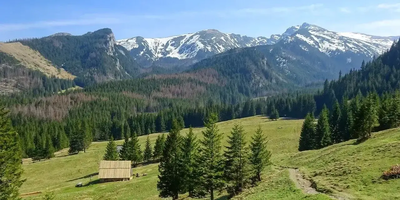 Piękne podkarpackie góry z ośnieżonymi szczytami, zielonymi halami i lasami. Na pierwszym planie drewniana szopa.
