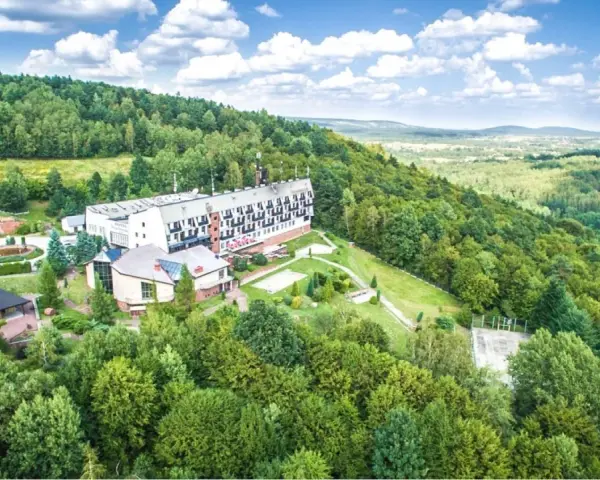 Hotel w otoczeniu zielonych lasów Gór Świętokrzyskich, blisko Kielc. Widok z lotu ptaka na budynki i krajobraz.