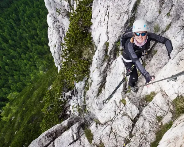 Kobieta wspina się po via ferrata w Dolomitach, z widokiem na gęsty las poniżej.