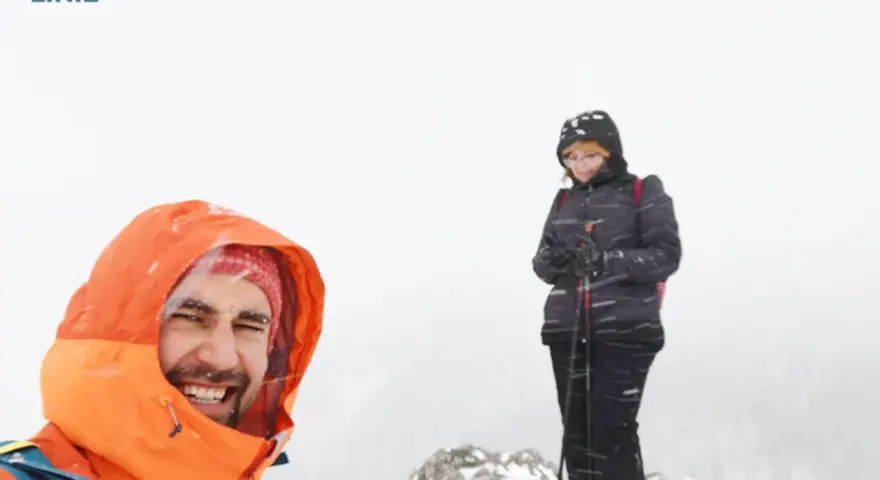 Uśmiechnięty turysta w pomarańczowej kurtce i kobieta z kijkami narciarskimi na tle mglistej doliny strążyskiej, blisko Sarniej Skały.