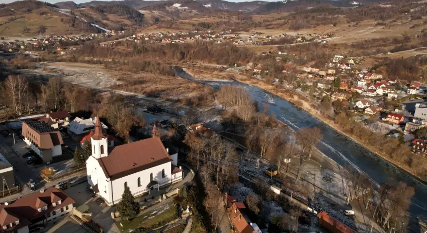 Widok z lotu ptaka na malowniczą dolinę Popradu zimą. Biały kościół z czerwoną wieżą góruje nad zabudowaniami.