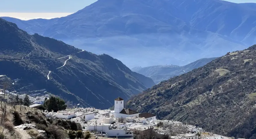Malownicza wioska w górach Sierra Nevada, Hiszpania, z białymi domami i kościołem, w tle błękitne pasma górskie.