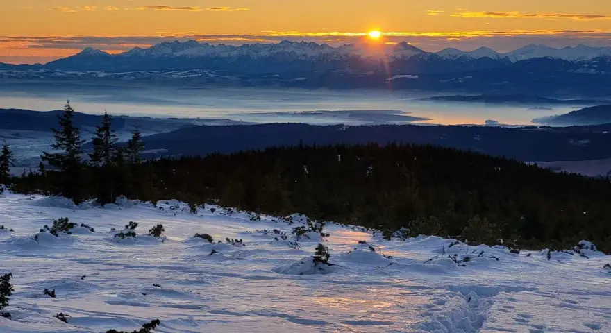 Zachód słońca nad mglistą doliną, ośnieżone szczyty górskie w tle. Odkryj mało znane miejsca na Pomorzu, gdzie zimowy krajobraz zapiera dech w piersiach.