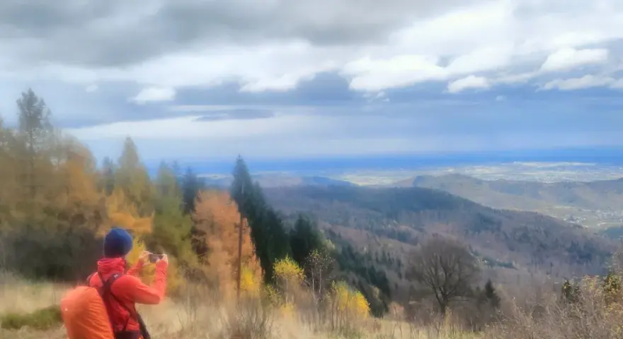 Widok na Beskid Mały jesienią. Turysta z pomarańczowym plecakiem fotografuje panoramę.