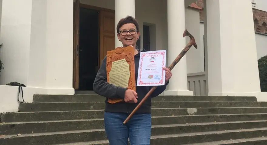 Uśmiechnięta kobieta z dyplomem i drewnianą laską, zdobywczyni Korony Gór Polskich.