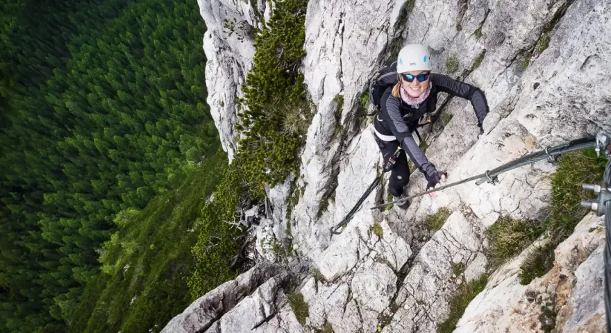 Kobieta wspina się po via ferrata w Dolomitach, z widokiem na gęsty las poniżej.